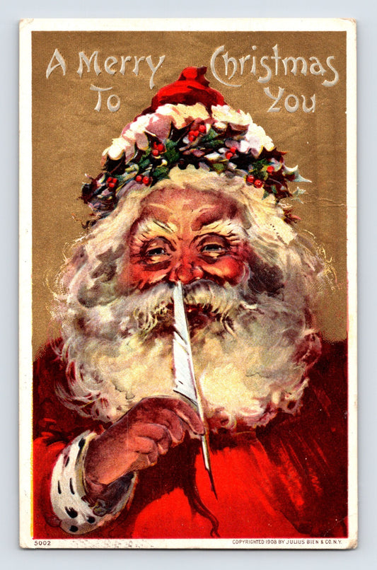 Close-up Santa Claus portrait holding a white feather quill beneath holly leaves and a red cap on this 1908 Julius Bien Christmas postcard.