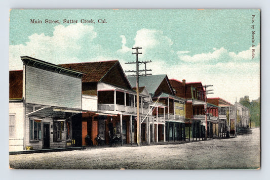 Sutter Creek California Main Street postcard showing early storefronts, wooden sidewalks, utility poles, and commercial buildings in a quiet Gold Country streetscape.