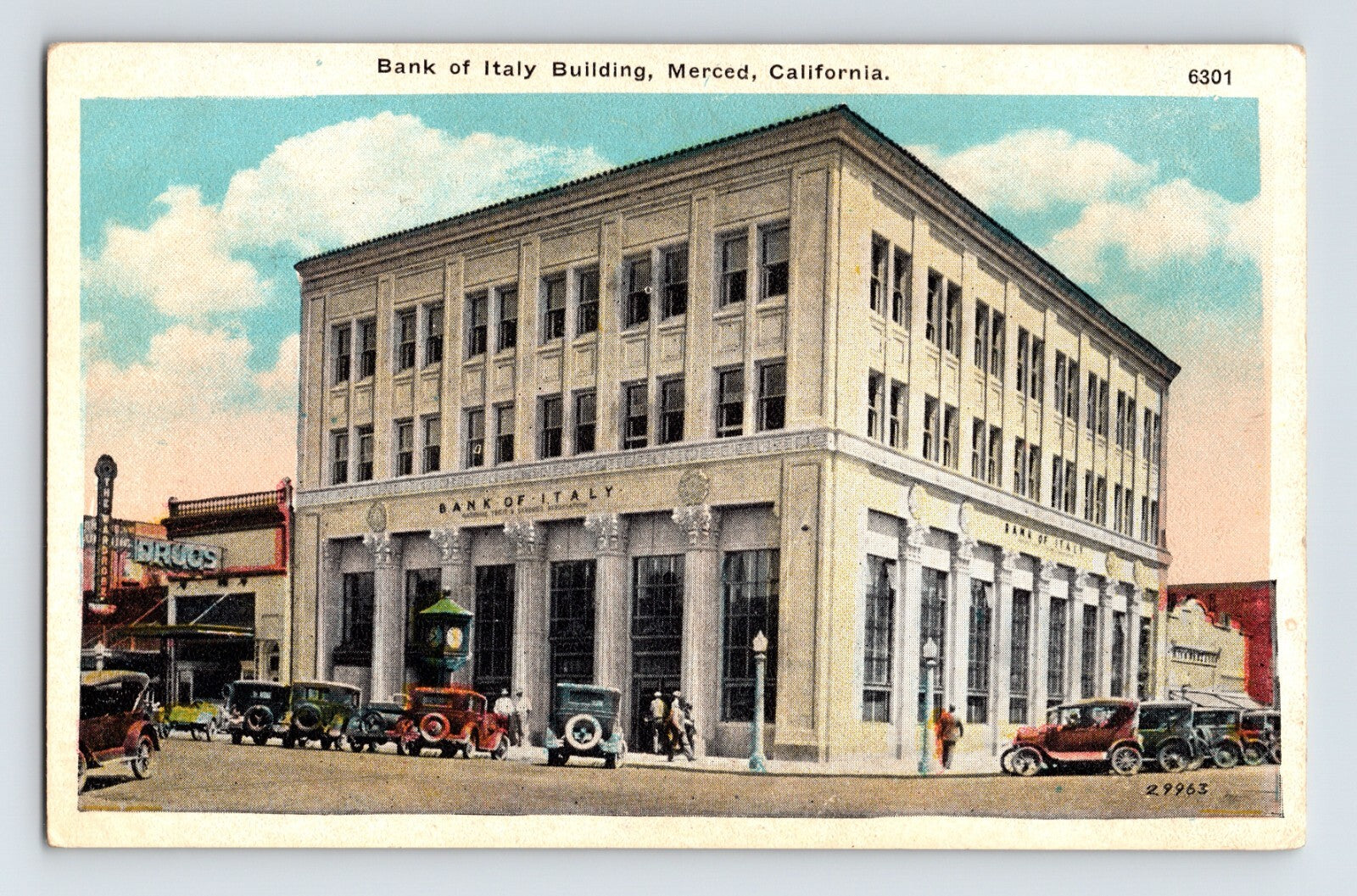 Postcard view of Bank of Italy Building in Merced, California, showing four-story neoclassical façade with early automobiles and storefronts along corner street.