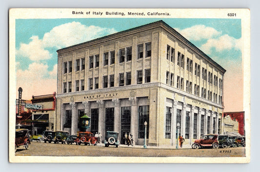 Postcard view of Bank of Italy Building in Merced, California, showing four-story neoclassical façade with early automobiles and storefronts along corner street.