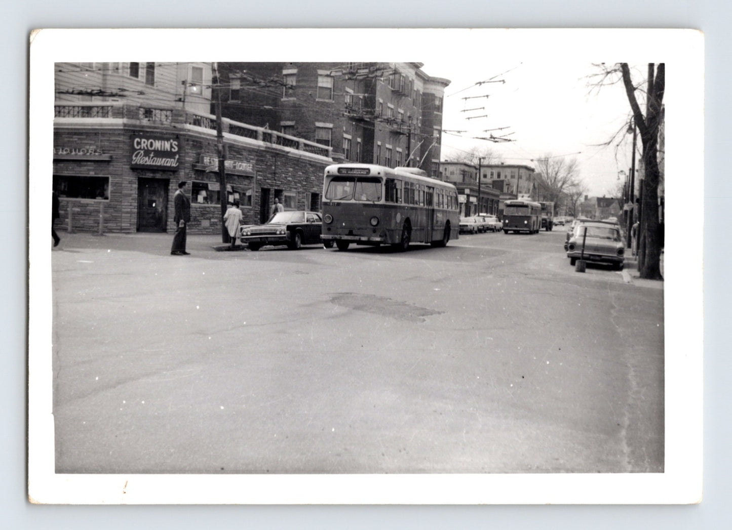 Massachusetts Bay Transportation Authority trackless trolley bus approaching Harvard Square in Cambridge Massachusetts with overhead electric wires and Cronin’s Restaurant visible on corner street scene, 1970s