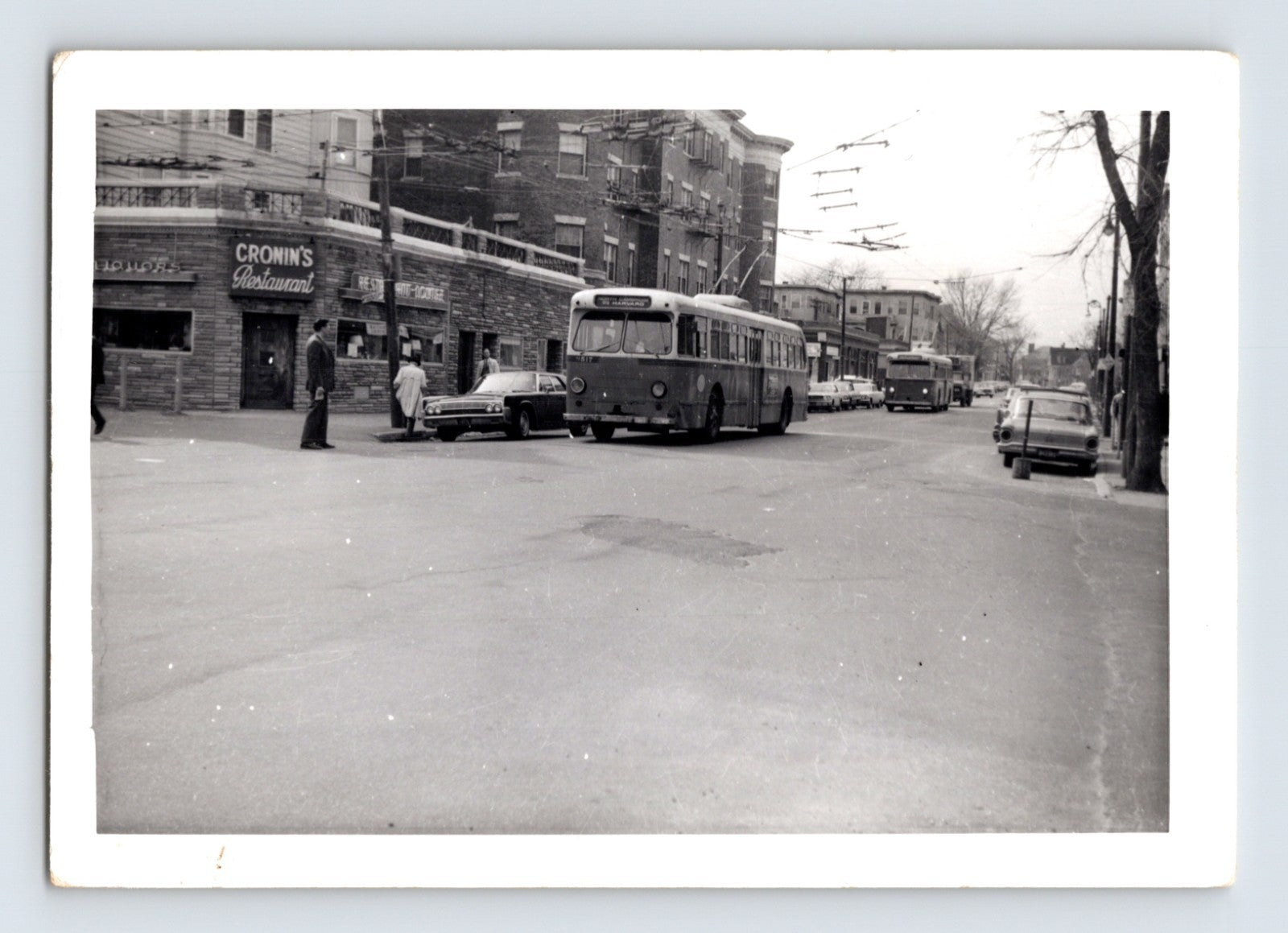 Massachusetts Bay Transportation Authority trackless trolley bus approaching Harvard Square in Cambridge Massachusetts with overhead electric wires and Cronin’s Restaurant visible on corner street scene, 1970s