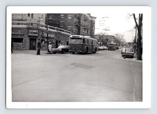 Massachusetts Bay Transportation Authority trackless trolley bus approaching Harvard Square in Cambridge Massachusetts with overhead electric wires and Cronin’s Restaurant visible on corner street scene, 1970s