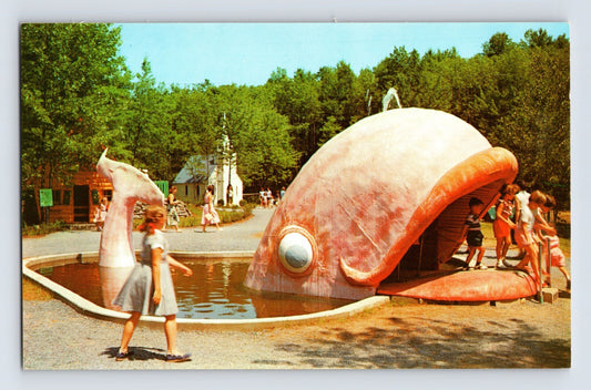 1960s chrome postcard showing the giant whale attraction at Storytown USA in Lake George, New York, with children entering the open whale mouth beside a small pond.