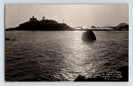 1930s Crescent City California lighthouse sunset real photo postcard showing silhouetted lighthouse on rocky island with reflective ocean foreground