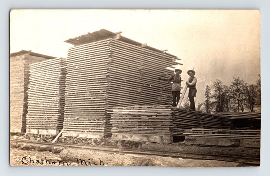 Chatham Michigan lumber yard 1907 real photo postcard stacks of milled boards men standing atop lumber piles rail siding scene