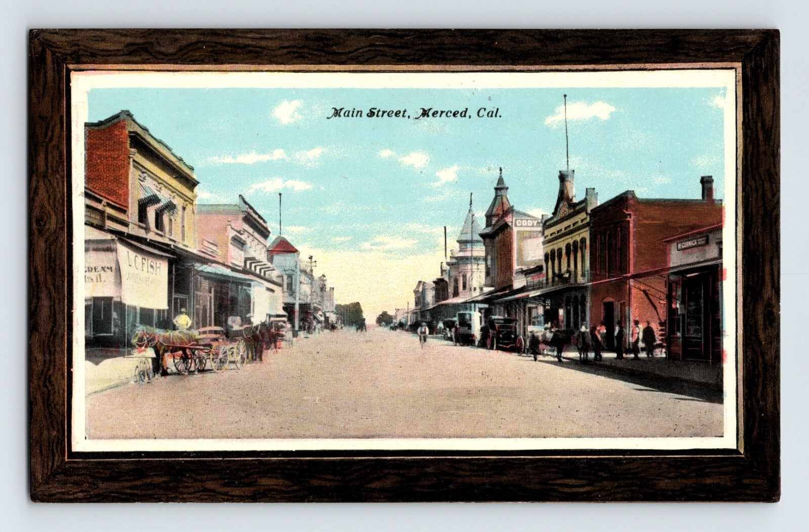 1911 postcard view of Main Street in downtown Merced, California, showing early commercial buildings, horse-drawn wagons, storefronts, and pedestrians along a wide unpaved street.