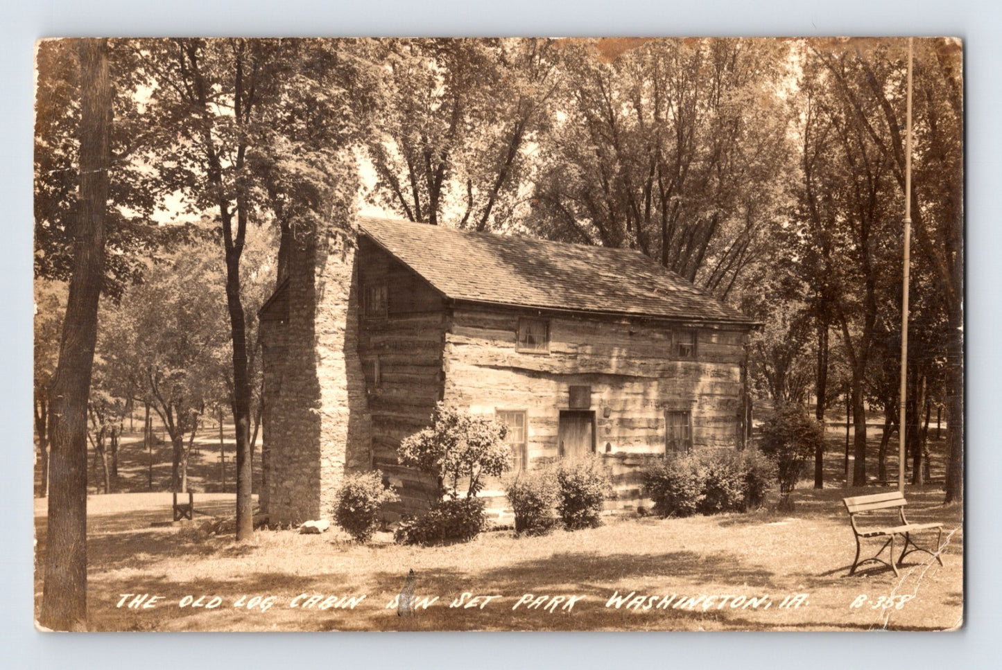 Old log cabin in Sunset Park Washington Iowa surrounded by trees real photo postcard
